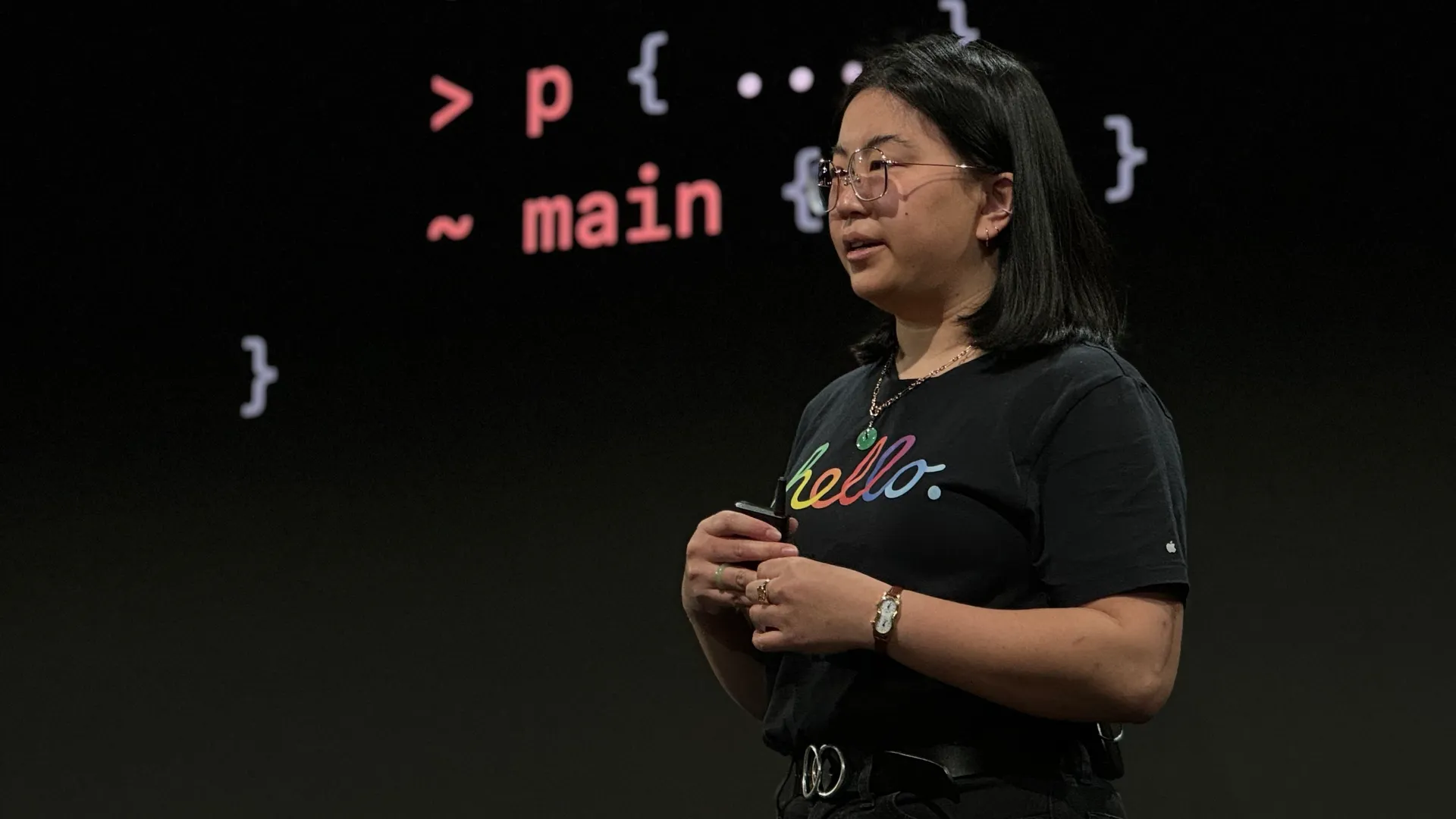 An Asian woman in a black t-shirt and glasses standing in front of a screen with a slide showing CSS selectors.