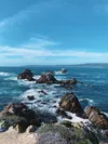The ocean waves crashing into the rocks along the shoreline of Point Lobos under a blue sky.