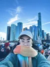 A woman in a beige cap and an orange/green scarf partially covering her face taking a selfie in front of Chicago’s waterfront.