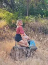 A blonde woman kneeling on a tree stump with her OneWheel in Sonora, California.