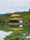 Kinkaku-ji, a golden Zen Buddhist shrine in Kyoko, surreounded by still water and green trees on a foggy day.