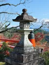 A stone lantern at Kurama-dera, framed by a vermilion wooden fence and the surrounding forested mountains.