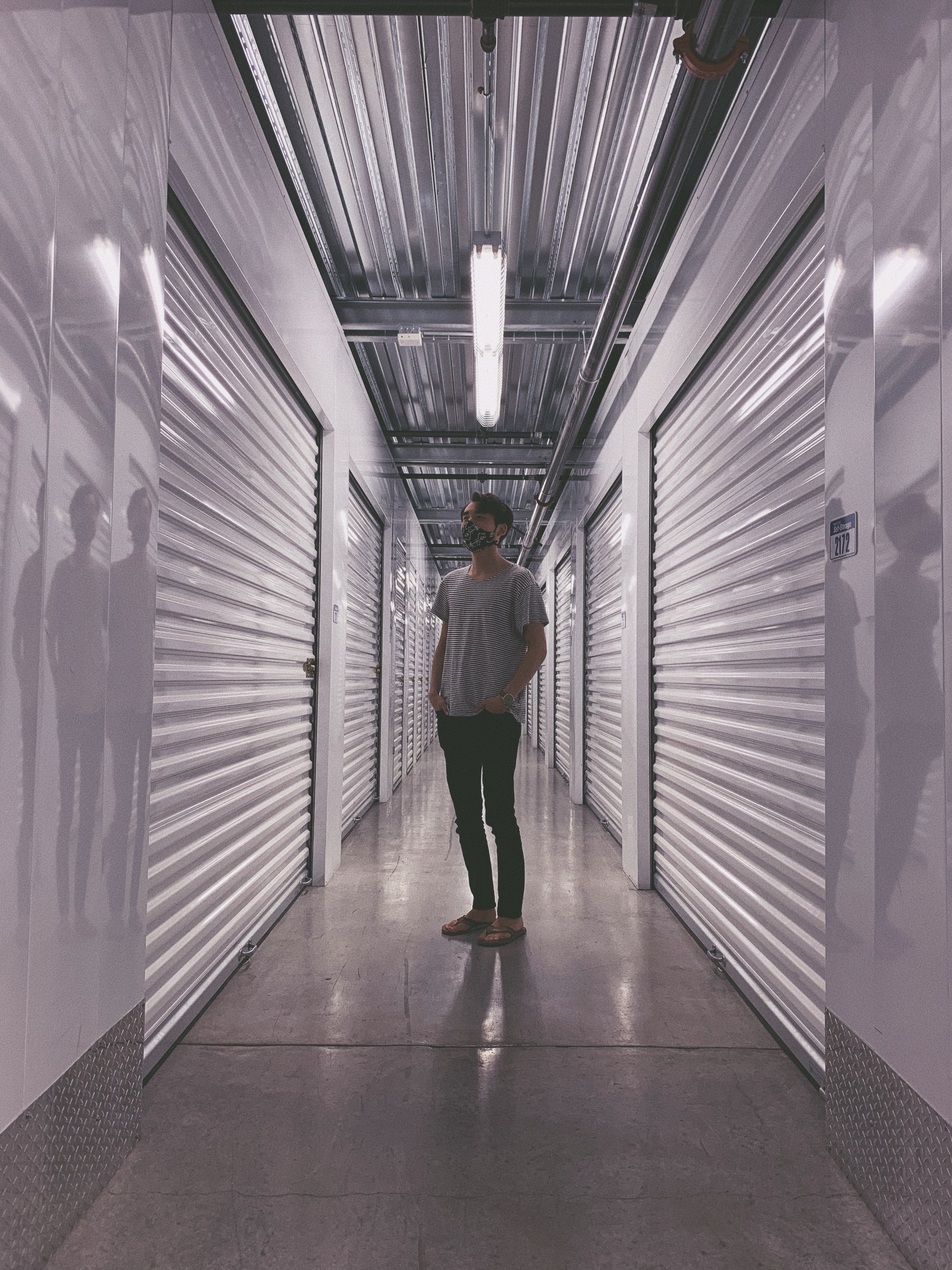A man in a striped shirt standing in the center of a long aisle of white metal storage units.
