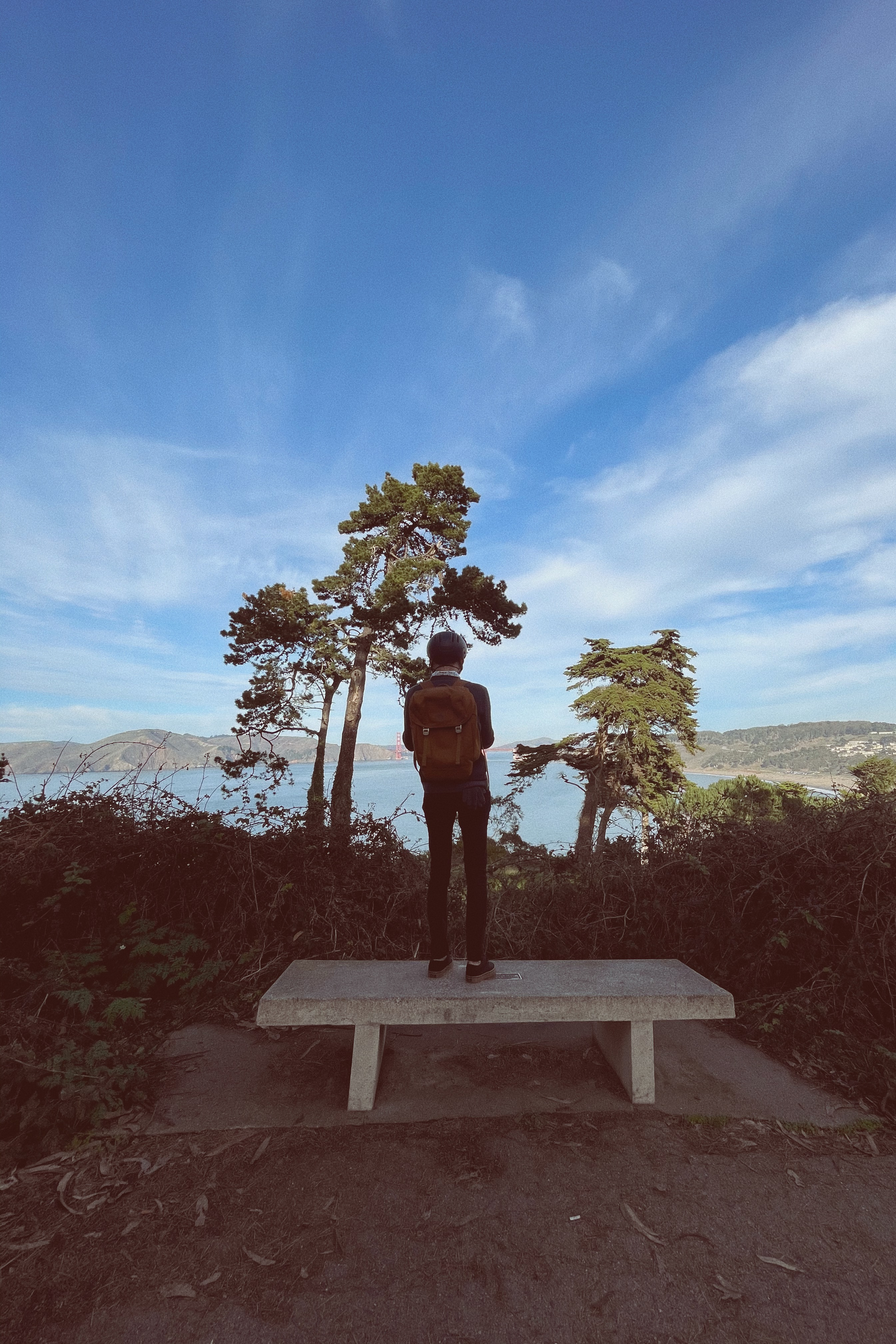 A man with a helmet and protective gear with his back to the camera, facing an overlook for the Golden Gate Bridge in San Francisco.