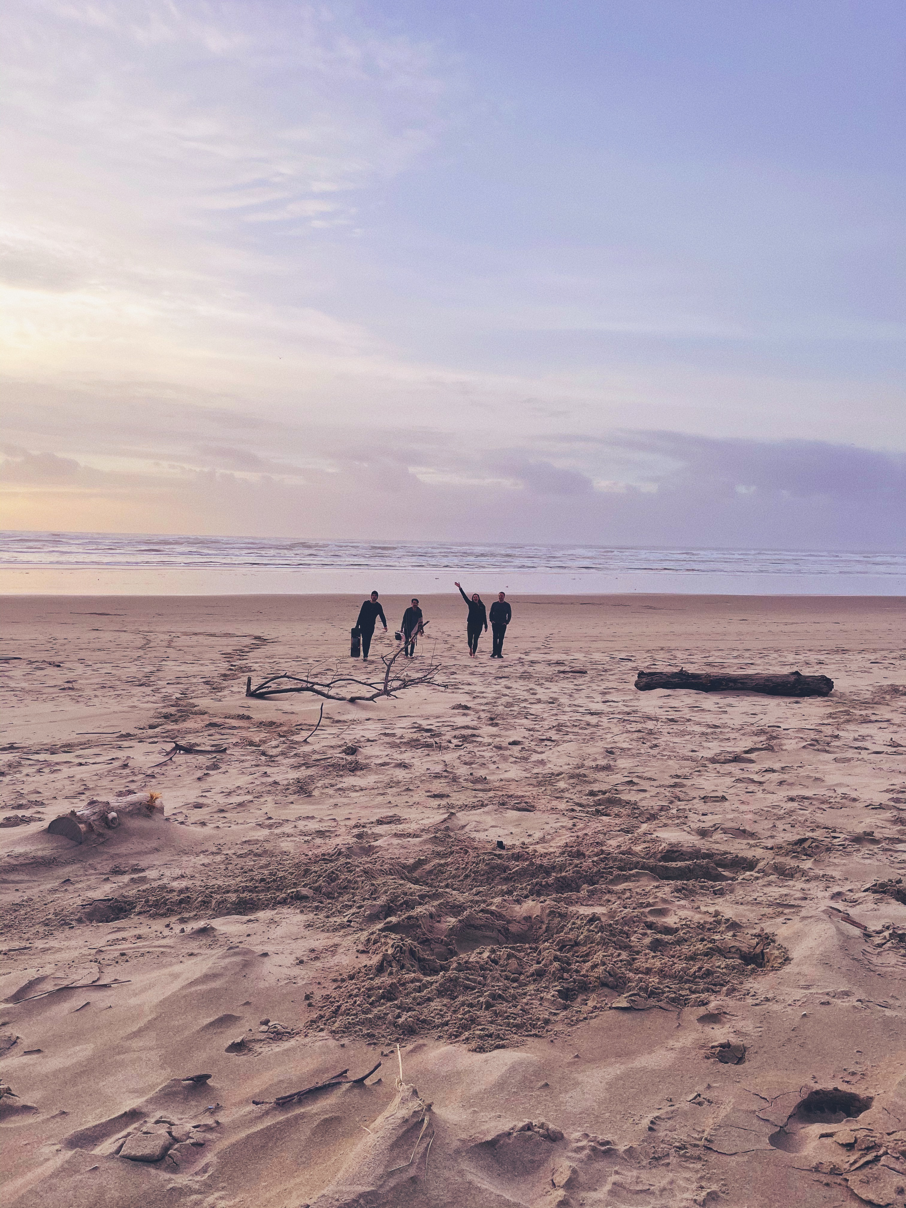 Four people in the distance walking towards the camera from the water’s edge at a beach in Waldport, Oregon.