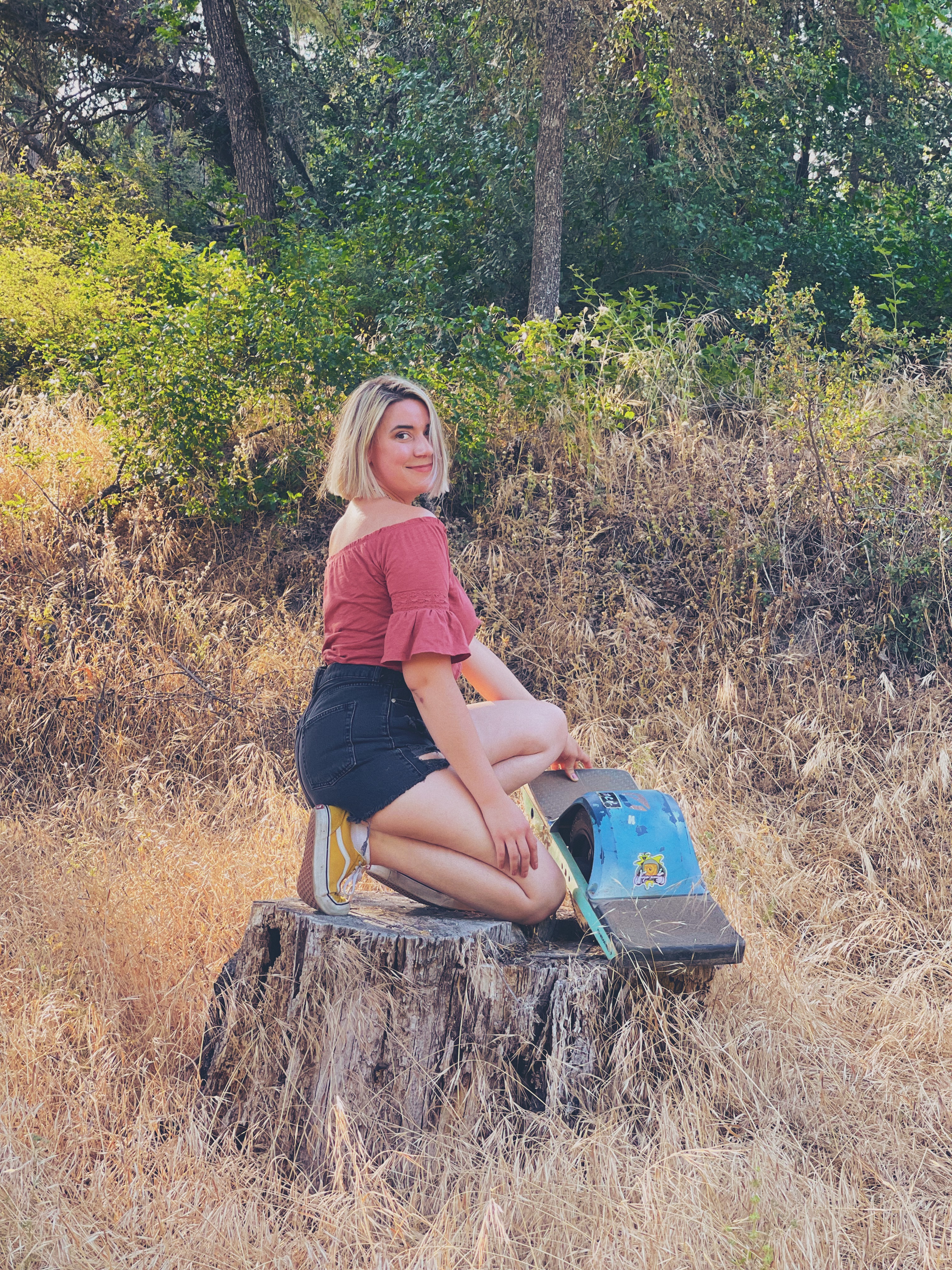 A blonde woman kneeling on a tree stump with her OneWheel in Sonora, California.