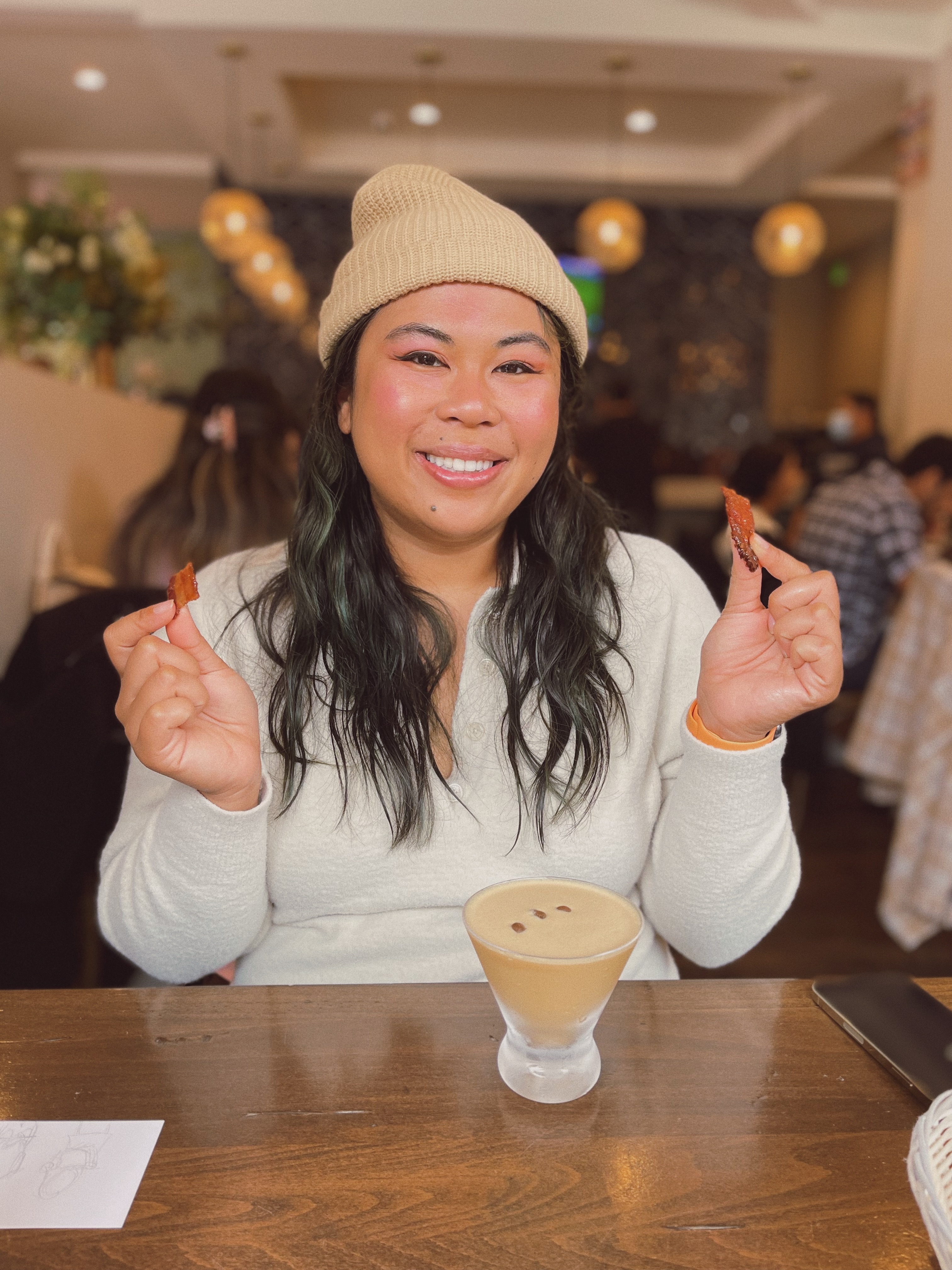 A person with long hair and beanie holding up pieces of bacon at a brunch restaurant in San Francisco.